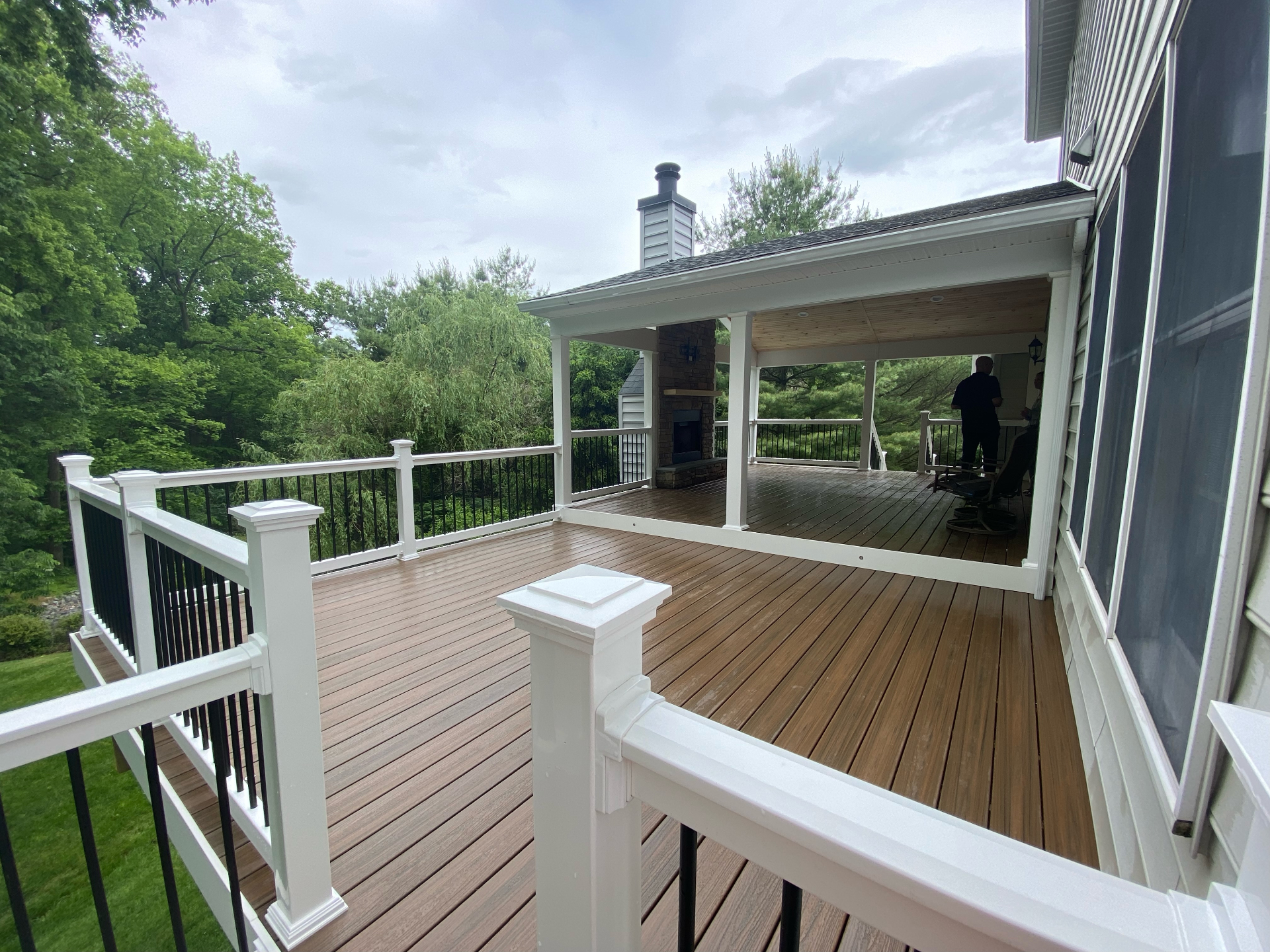 Covered deck with fireplace and wooded backyard view